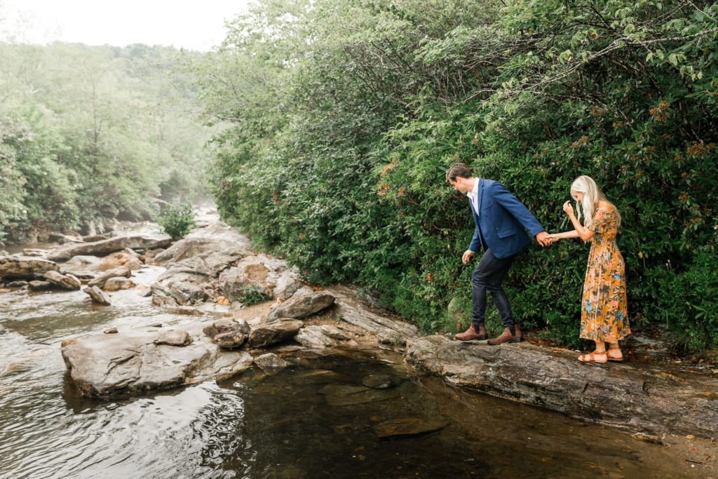 Engaged couple crossing a river in the blue ridge mountains.