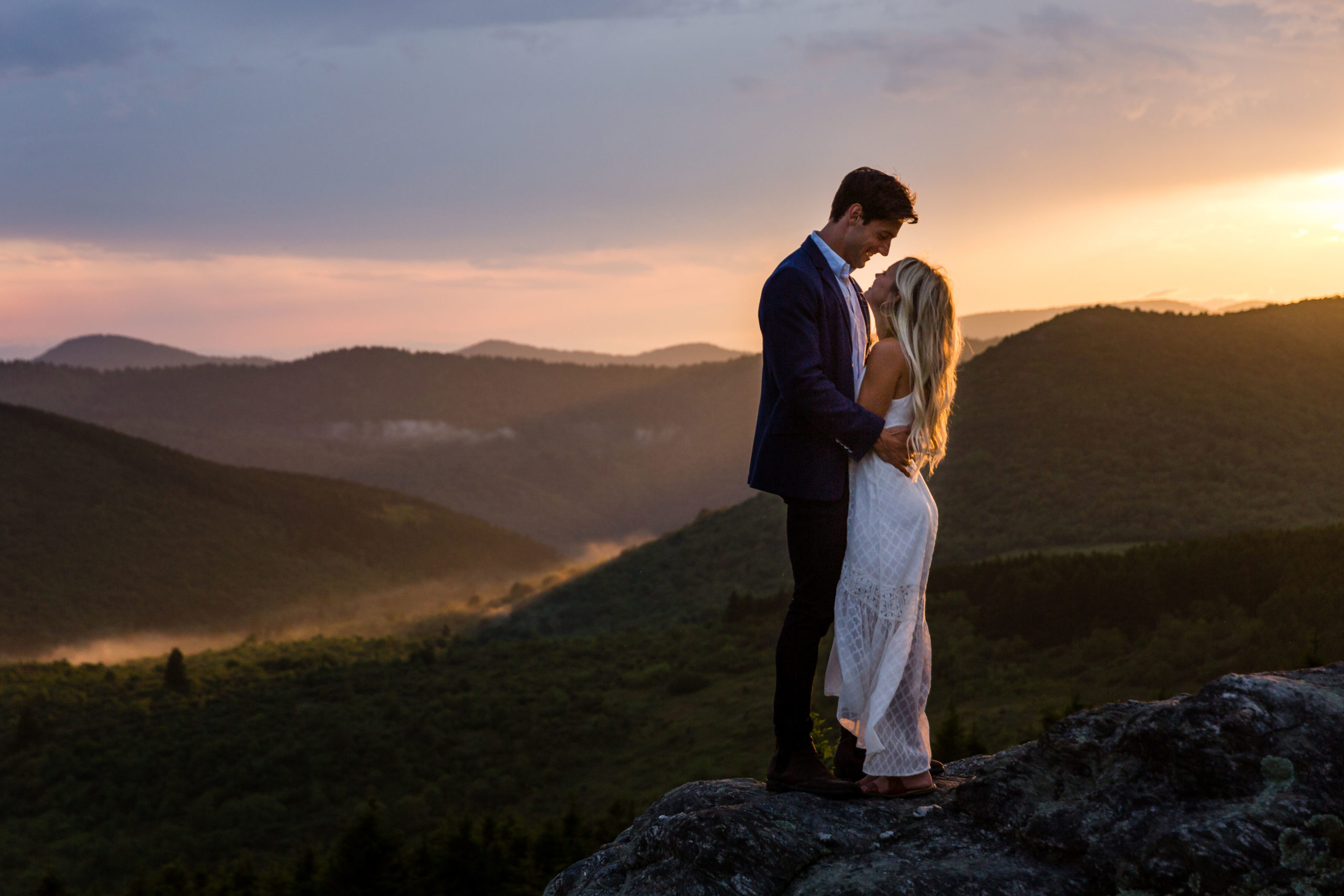 Engaged couple embrace in front of a beautiful mountain backdrop.