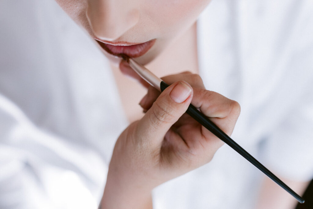 Close-up detail of a bride’s lips as a makeup artist applies lipstick for her finishing wedding-day makeup.