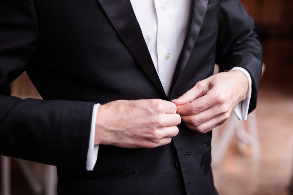 closeup photo of Groom buttoning the top button of his black tux