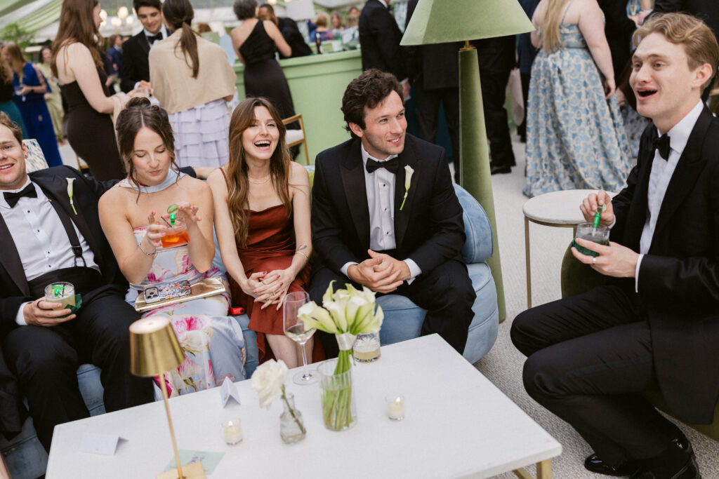 Wedding guests in formal attire laughing and enjoying cocktails inside an elegant tented wedding reception with custom lounge seating and luxury event design.