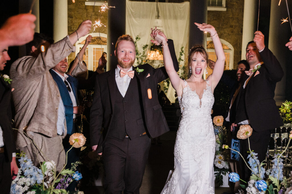 Bride and groom exit their wedding with hands in the air being cheered on by guests.