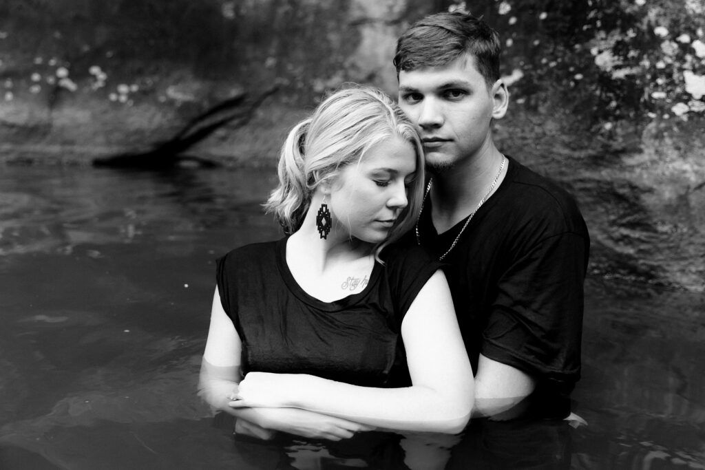 A black and white photo of an engaged couple wear matching black t-shirts to plunge into a secret swimming hole in the mountains of North Carolina.